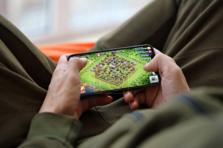 Photo for Clash of Clans mobile iOS game on iPhone 15 smartphone screen in male hands during mobile gameplay. Mobile gaming and entertainment on portable device - Royalty Free Image
