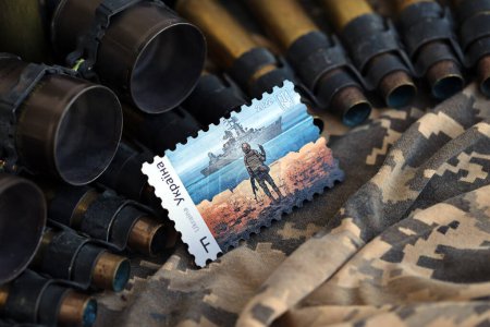 Photo for TERNOPIL, UKRAINE - SEPTEMBER 29, 2023 Famous Ukrainian postmark with russian warship and ukrainian soldier as wooden souvenir on army camouflage uniform cloth and machine gun belt shells - Royalty Free Image