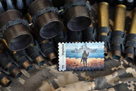 Photo for TERNOPIL, UKRAINE - SEPTEMBER 29, 2023 Famous Ukrainian postmark with russian warship and ukrainian soldier as wooden souvenir on army camouflage uniform cloth and machine gun belt shells - Royalty Free Image