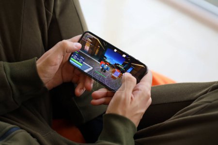 Téléchargez les photos : Roblox jeu iOS mobile sur iPhone 15 écran de smartphone dans les mains des hommes pendant le gameplay mobile. Jeux mobiles et divertissement sur appareil portable - en image libre de droit