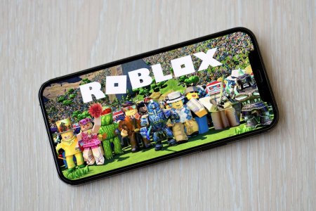 Photo for Roblox mobile iOS game on iPhone 15 smartphone screen on wooden table during mobile gameplay. Mobile gaming and entertainment on portable device - Royalty Free Image