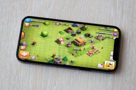 Photo for Clash of Clans mobile iOS game on iPhone 15 smartphone screen on wooden table during mobile gameplay. Mobile gaming and entertainment on portable device - Royalty Free Image