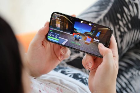 Téléchargez les photos : Roblox jeu iOS mobile sur iPhone 15 écran de smartphone entre les mains des femmes pendant le gameplay mobile. Jeux mobiles et divertissement sur appareil portable - en image libre de droit