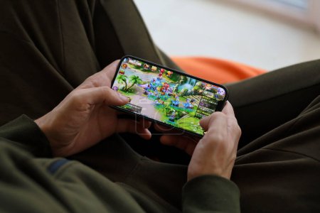 Foto de Fantasy Westward Journey juego iOS móvil en la pantalla del teléfono inteligente iPhone 15 en manos masculinas durante el juego móvil. Juegos móviles y entretenimiento en dispositivos portátiles - Imagen libre de derechos