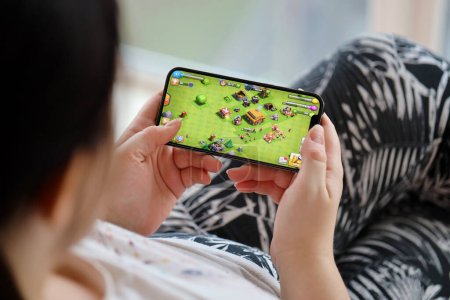 Photo for Clash of Clans mobile iOS game on iPhone 15 smartphone screen in female hands during mobile gameplay. Mobile gaming and entertainment on portable device - Royalty Free Image