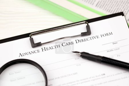 Téléchargez les photos : Directive préalable sur les soins de santé formulaire vierge sur tablette A4 se trouve sur la table de bureau avec stylo et loupe gros plan - en image libre de droit