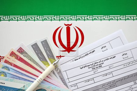 Photo for Iranian annual income tax return form F20-25-006 ready to fill on table with pen and iranian money on flag close up - Royalty Free Image
