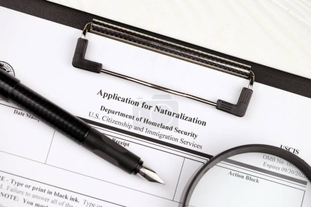 Photo for N-400 Application for Naturalization blank form on A4 tablet lies on office table with pen and magnifying glass close up - Royalty Free Image