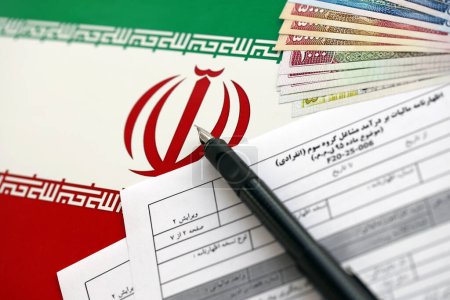 Photo for Iranian annual income tax return form F20-25-006 ready to fill on table with pen and iranian money on flag close up - Royalty Free Image