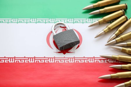 Photo for Small padlock lies on pile of iranian flag and rifle bullets close up. Sanctions, ban or embargo due to armed terror concept - Royalty Free Image