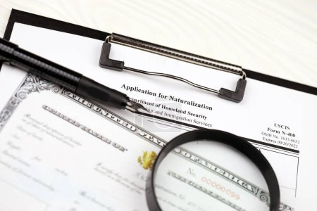 Photo for N-400 Application for Naturalization and Certificate of naturalization on A4 tablet lies on office table with pen and magnifying glass close up - Royalty Free Image