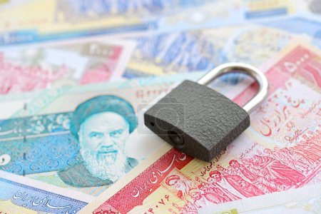 Kleines Vorhängeschloss liegt auf einem Haufen iranischen Geldes in Großaufnahme. Sanktionen, Verbot oder Embargo-Konzept
