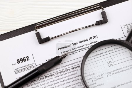 Téléchargez les photos : IRS Form 8962 Premium tax cerdit PTC blanc sur tablette A4 se trouve sur la table de bureau avec stylo et loupe close up - en image libre de droit