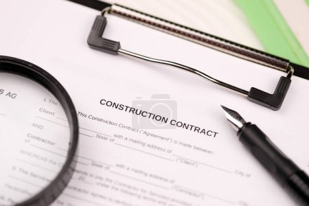 Construction contract form on A4 tablet lies on office table with pen and magnifying glass close up