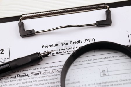 Téléchargez les photos : IRS Form 8962 Premium tax cerdit PTC blanc sur tablette A4 se trouve sur la table de bureau avec stylo et loupe close up - en image libre de droit