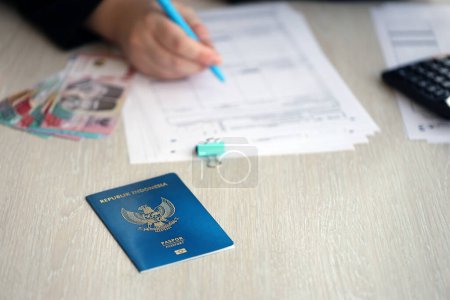 Photo for Indonesia passport and service workers table on process of citizenship registration. Female worker fills papers of citizenship - Royalty Free Image