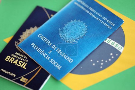 Passport of Brazil and work card with brazilian reais money bills on flag background close up