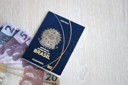Passport book of Federative Republic of Brazil and brazilian reais money bills on wooden background close up