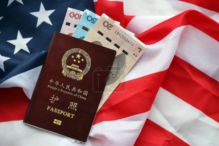 Red passport of People Republic of China and chinese yuan money bills on United States flag. PRC chinese passport on bright background close up