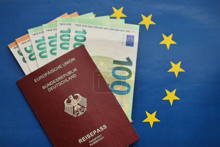 Red German passport of European Union and money on blue flag background close up. Tourism and citizenship concept
