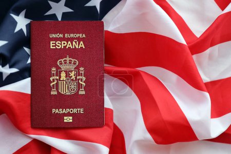 Red Spanish passport of European Union on United States national flag background close up. Tourism and diplomacy concept