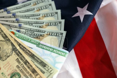 Permanent Resident United States of America Green Card and dollar bills on folded US flag close up