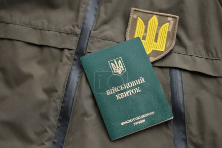 Military token or army ID ticket lies on green ukrainian military uniform indoors close up