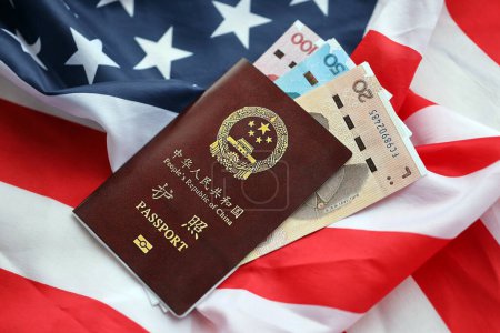 Roter Pass der Volksrepublik China und chinesische Yuan-Geldscheine auf der Flagge der Vereinigten Staaten. Chinesischer Pass der Volksrepublik China auf hellem Hintergrund in Nahaufnahme
