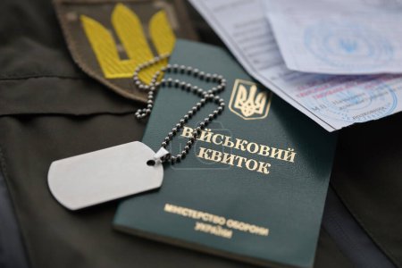 Militärmarke oder Armeeausweis mit Mobilisierungsbescheid liegt auf grüner ukrainischer Militäruniform drinnen in Großaufnahme