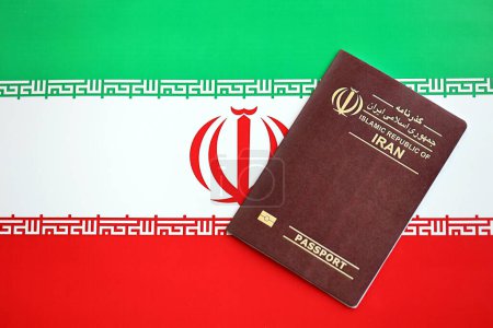 Red Islamic Republic of Iran passport on national flag background close up. Tourism and citizenship concept
