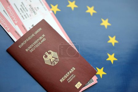 Red German passport of European Union and airlines tickets on blue flag background close up. Tourism and travel concept