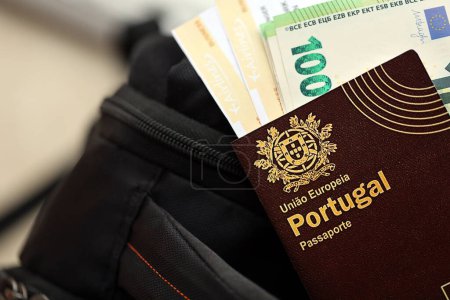 Pasaporte rojo de Portugal de la Unión Europea con billetes de avión y dinero en mochila turística de cerca. Concepto de turismo y viajes