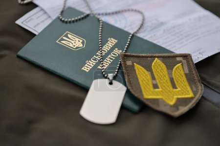 Military token or army ID ticket with mobilization notice lies on green ukrainian military uniform indoors close up