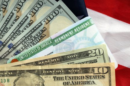Residente Permanente Estados Unidos de América Tarjeta Verde y billetes de dólar en bandera estadounidense plegada de cerca