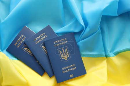 Three Ukrainian biometrical passports on folded waving flag of Ukraine country close up