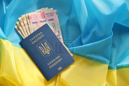 Un passeport biométrique ukrainien et des factures de hryvnia UAH sur le drapeau ondulé plié du pays d'Ukraine gros plan