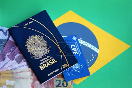 Reisepass der Föderativen Republik Brasilien, CPF-Steuerkarte und brasilianische Reais-Geldscheine auf Fahnenhintergrund in Großaufnahme
