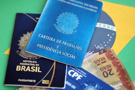 Passport of Brazil, CPF taxpayer card and work card with brazilian reais money bills on flag background close up