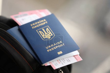 Zwei ukrainische biometrische Pässe mit Flugtickets auf schwarzem Touristenrucksack in Großaufnahme