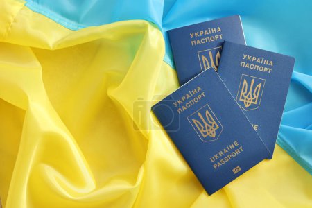 Tres pasaportes biométricos ucranianos en la bandera ondeante plegada del país de Ucrania de cerca