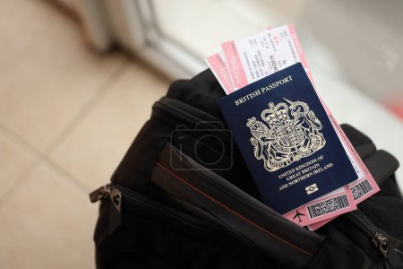 Blue British passport with airline tickets on touristic backpack close up. Tourism and travel concept