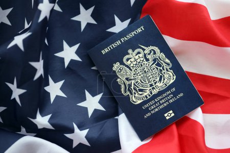 Blue British passport on United States national flag background close up. Tourism and diplomacy concept