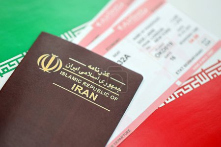 Red Islamic Republic of Iran passport with airline tickets on Iranian flag background close up. Tourism and travel concept