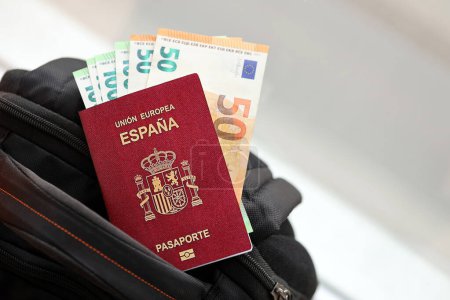Pasaporte rojo español de la Unión Europea con billetes de avión y dinero en mochila turística de cerca. Concepto de turismo y viajes