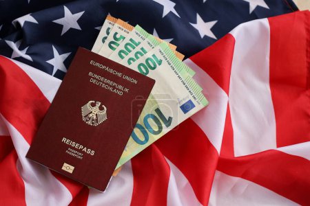 Red German passport of European Union and money on United States national flag background close up. Tourism and diplomacy concept