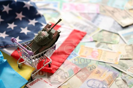 Foto de Tanque de juguete en bandera estadounidense y bandera ucraniana en muchos billetes de diferentes monedas. Antecedentes de financiación de la guerra y apoyo militar entre Estados Unidos y Ucrania - Imagen libre de derechos