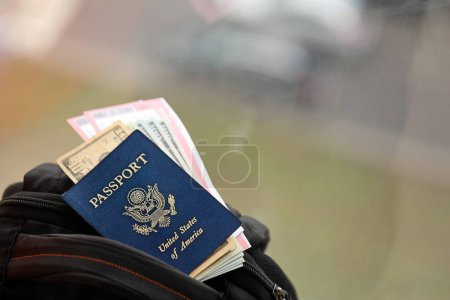 Pasaporte azul de los Estados Unidos de América con billetes de avión y dinero en mochila turística de cerca. Concepto de turismo y viajes