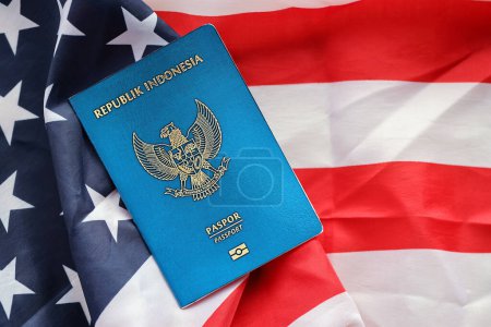 Pasaporte de la República Azul Indonesia en el fondo de la bandera nacional de los Estados Unidos de cerca. Concepto de turismo y diplomacia