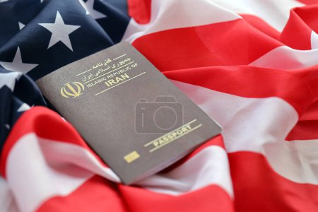 Red Islamic Republic of Iran passport on United States national flag background close up. Tourism and diplomacy concept