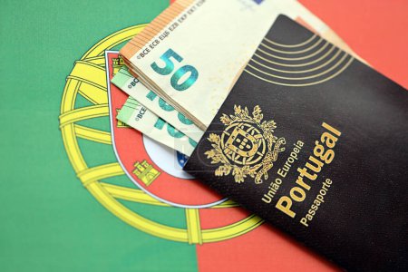 Red Portugal passport of European Union and money on flag background close up. Tourism and citizenship concept